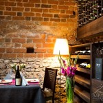 Zdjęcia przedstawiają wnętrza restauracji. Stolik dla dwóch osób w piwniczce z winami.